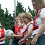Women smiling and laughing while playing net ball.