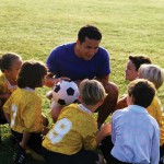 A football coaching giving a pep talk to a young team of boys and girls.